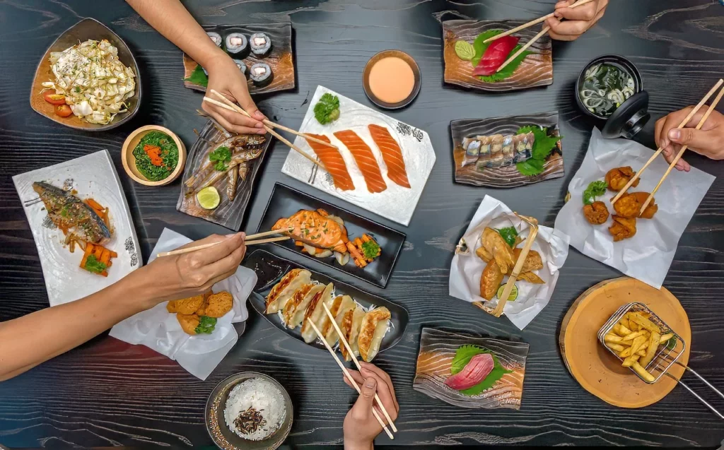 People eating various Japanese dishes on wooden table, showcasing Japan's food and drink culture.